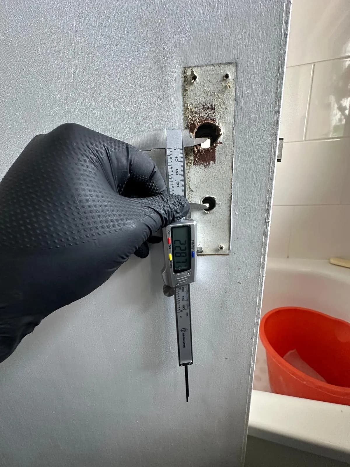 A gloved hand using a tool to measure a door lock case.