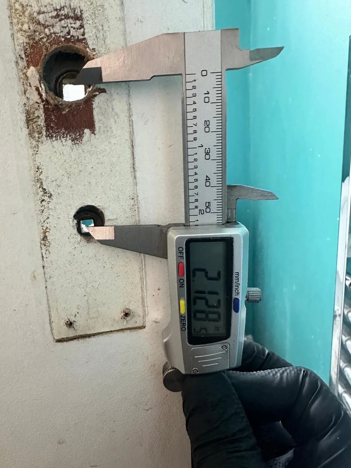 A digital caliper checking a lock opening in a door.