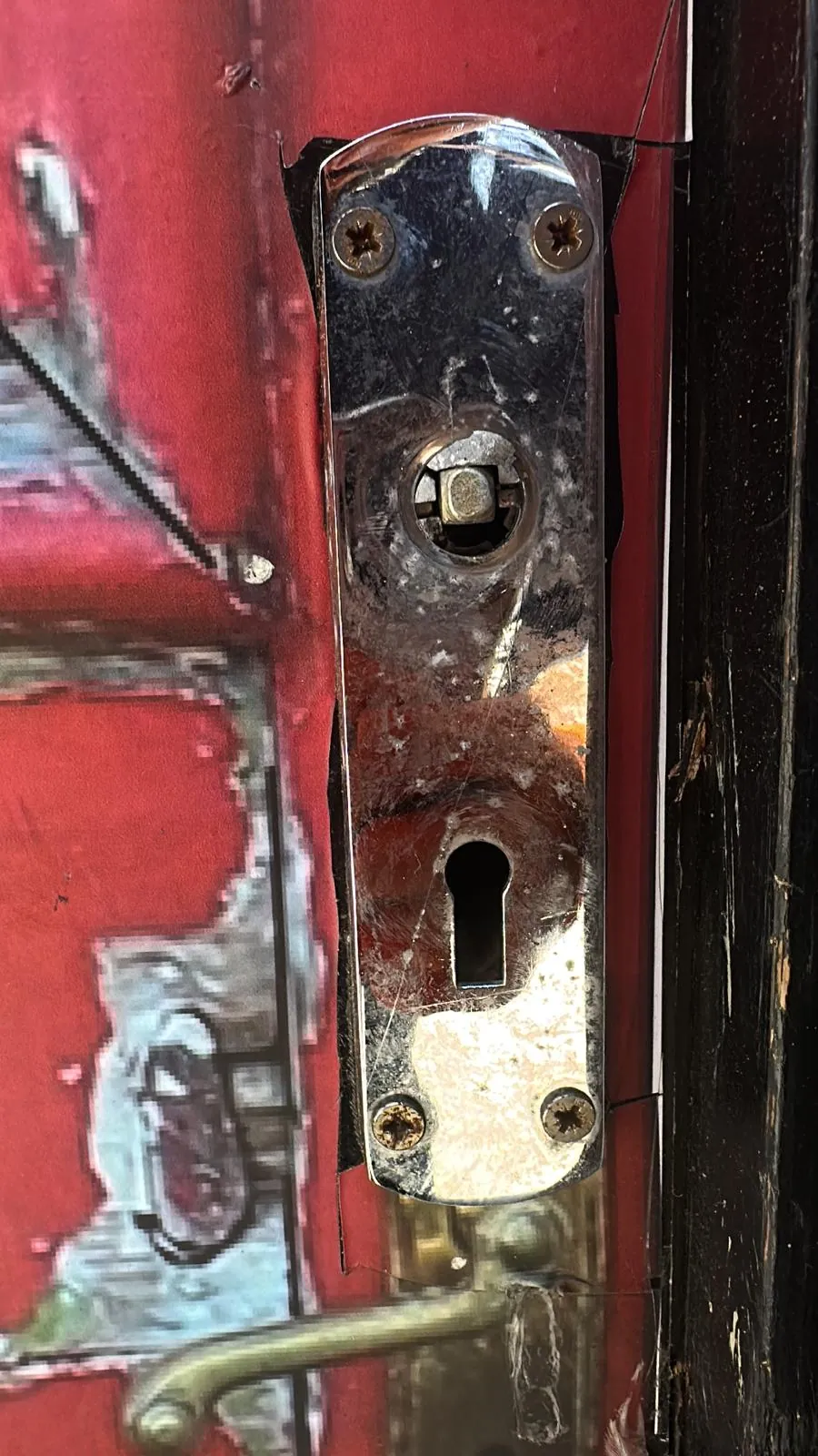 A worn red door with older lock fittings and a keyhole.
